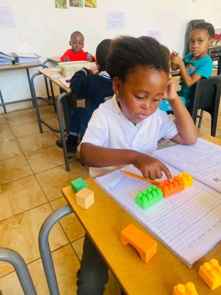 A learner counting with building blocks beside her workbook