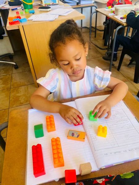 A learner placing building blocks on an open workbook