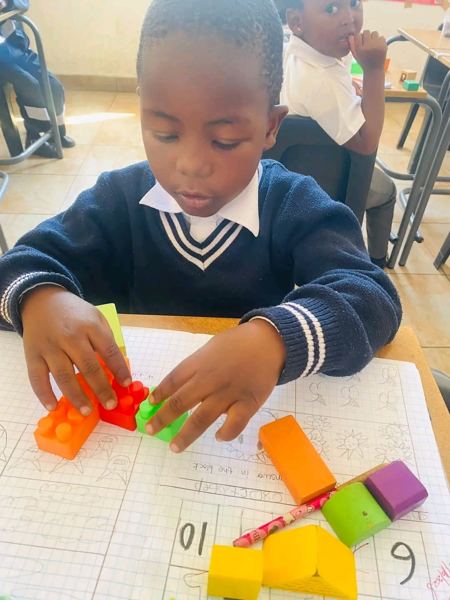 A learner in school uniform stacking blocks to solve a sum